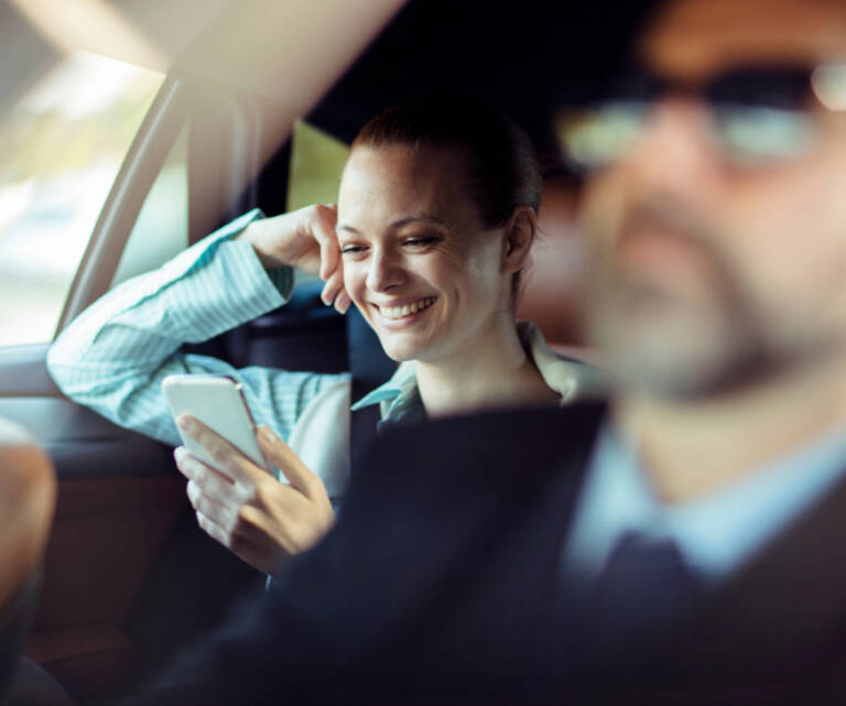 Smiling woman using phone in luxury black SUV during long-distance VIP transfer with professional chauffeur