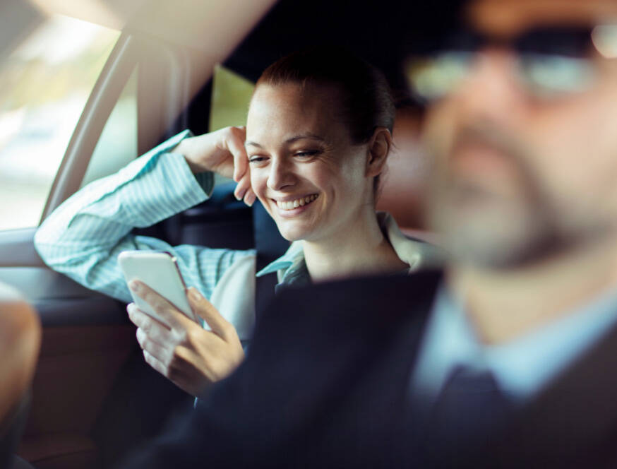 Smiling woman using phone in luxury black SUV during long-distance VIP transfer with professional chauffeur